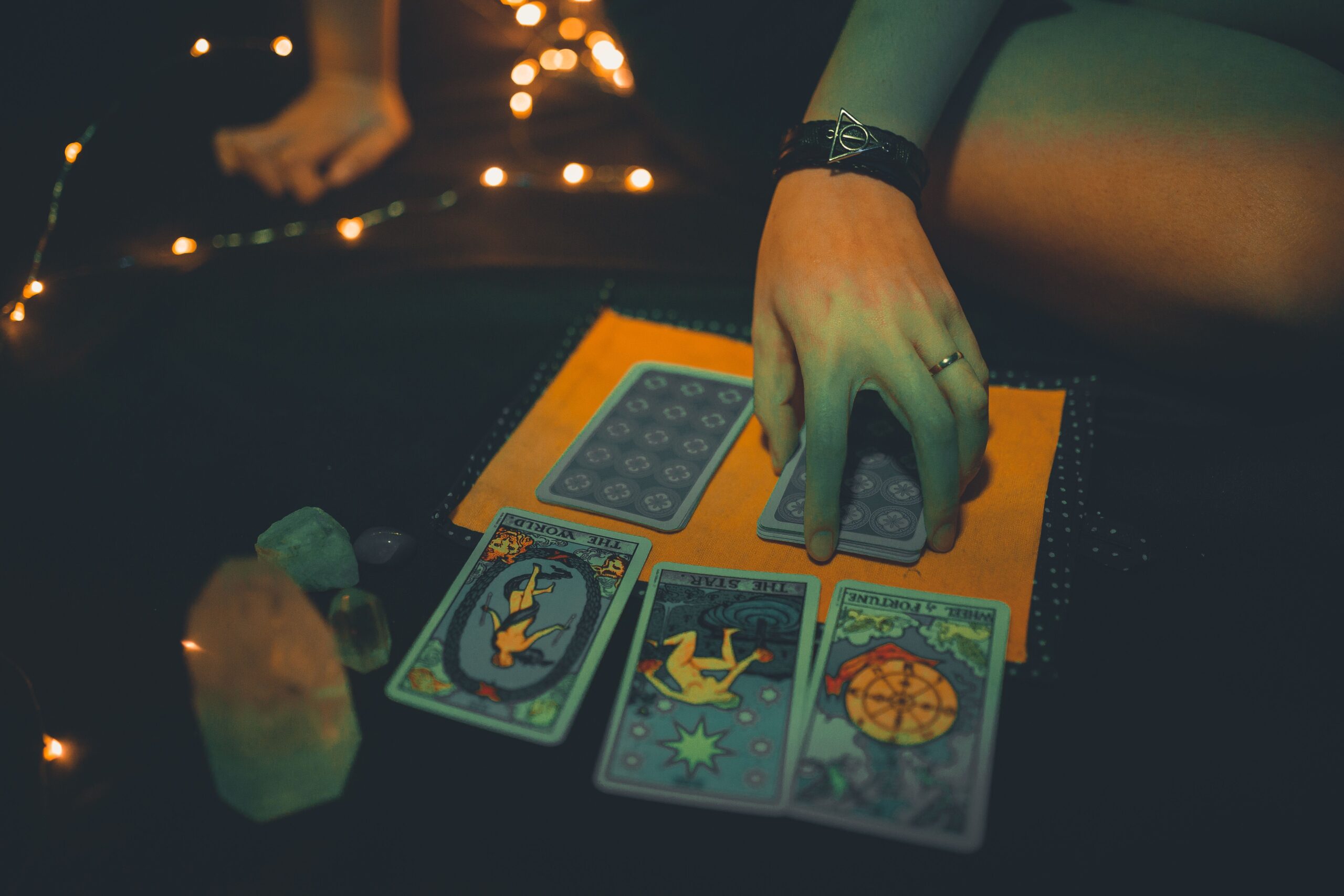 From above crop anonymous female using tarot cards on table and fortunetelling in dark room